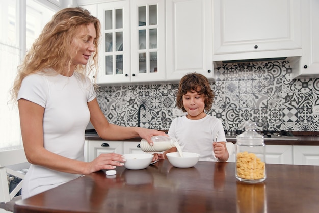 Schöne Mutter gießt Milch in einen Teller mit Müsli Schöne Mutter bereitet Frühstück für ihren geliebten Sohn vor