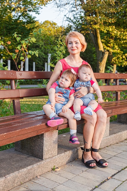 Schöne Mutter mit ihrer Tochter und ihrem Sohn sitzt im Sommer auf einer Bank im Park