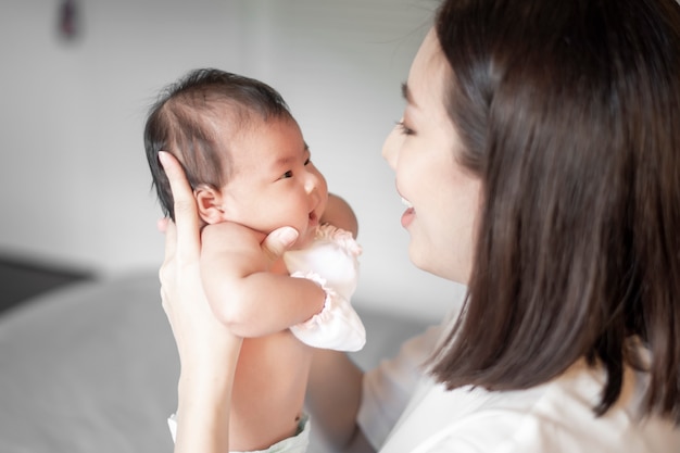 Schöne Mutter spielt mit ihrem neugeborenen Baby im Schlafzimmer.