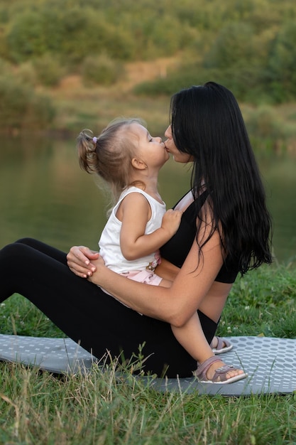 Schöne Mutter und ihre süße Tochter küssen sich liebevoll, während sie sich im Freien ansehen
