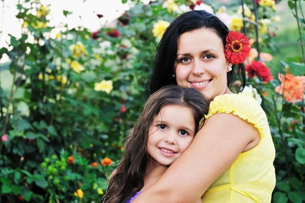 schöne mutter und tochter im freien im garten zusammen mit blumen haben spaß und umarmung