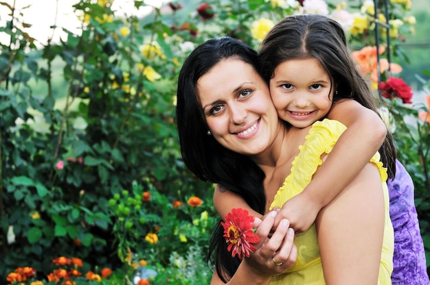 schöne mutter und tochter im freien im garten zusammen mit blumen haben spaß und umarmung