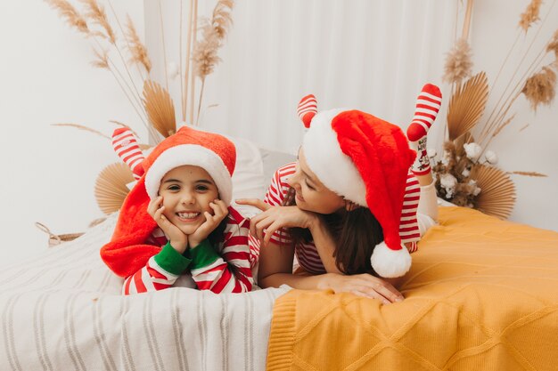 Schöne Mutter und Tochter im Weihnachtspyjama umarmen und spielen zu Hause im Schlafzimmer auf dem Bett. Weihnachten