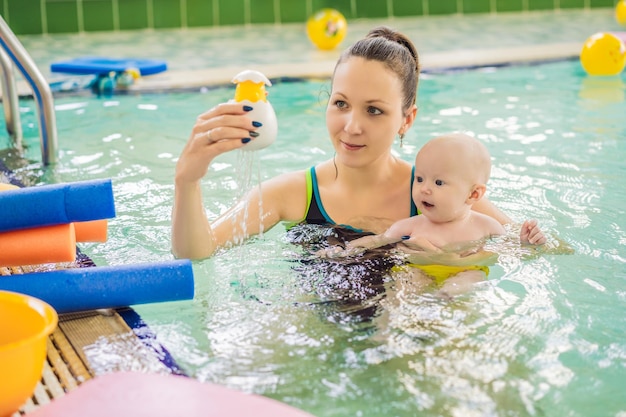 Schöne Mutter unterrichtet ein süßes Baby, wie man im Schwimmbad schwimmt.