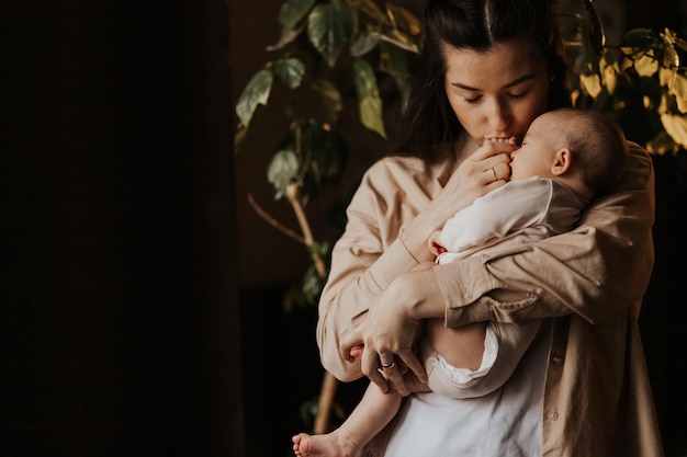 Schöne Mutter unterstützt und kuschelt zärtlich das neugeborene Baby Hübsche Mutter, die mit Liebe aussieht und Schutz zeigt