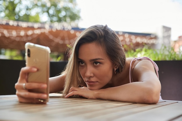 Schöne nachdenkliche melancholische asiatische Dame, die im Café liegt, mit Smartphone