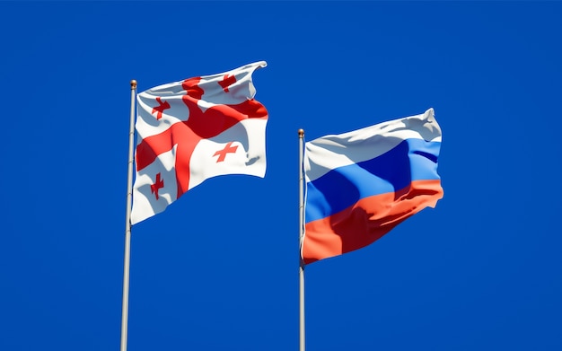 Schöne Nationalstaatsflaggen von Georgien und von Russland zusammen auf blauem Himmel. 3D-Grafik