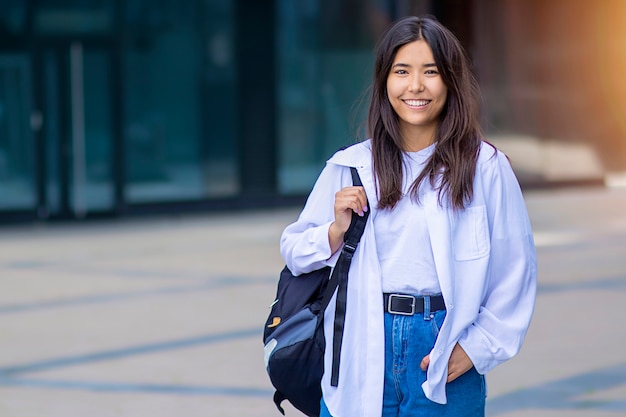 Schöne nette asiatische Frau oder junges Mädchen, das breit mit Rucksack lächelt. Freudige Dame im Freien. Student draußen im weißen Hemd. Speicherplatz kopieren.