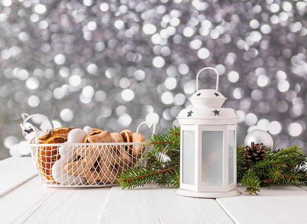 Schöne Neujahrs- und Weihnachtskomposition mit einer weißen Laterne, einem Korb mit glasiertem Lebkuchen und getrockneten Orangenscheiben, Fichtenzweigen, Bokeh