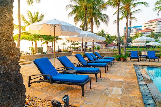 schöne Palme mit Sonnenschirm Stuhl Pool im Luxushotel Resort zu Sonnenaufgang Zeiten - Urlaub und Urlaubskonzept