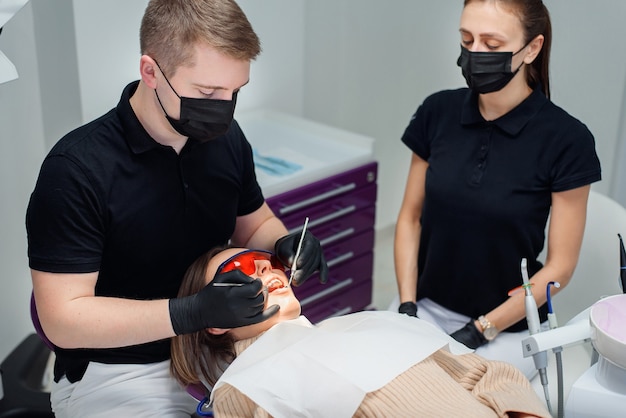 Schöne Patientin in der roten Schutzbrille in einem Zahnarztstuhl an der modernen stilvollen Klinik.