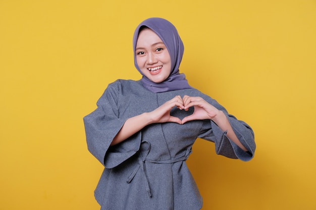 Schöne positive, freundlich aussehende junge Frau, die Hijab mit einem schönen aufrichtigen Lächeln trägt und sich dankbar und dankbar fühlt, gibt Liebesgeste