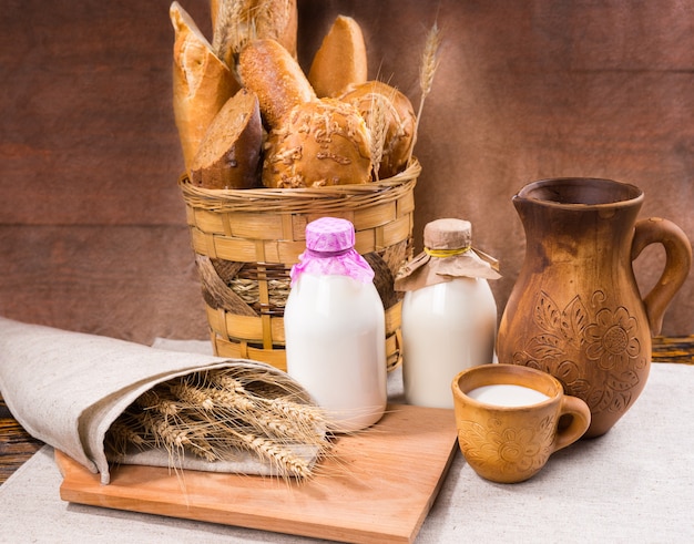 Schöne Präsentation von Landbrot in einem geflochtenen Korb und wispigen Körnern, eingewickelt in Leinen neben Milchflaschen und einem Holzkrug