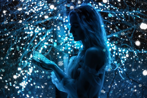 Schöne Prinzessin im blauen langen Kleid auf dem leuchtenden Baumhintergrund mit Kristallschuh in der Hand. Kunstverarbeitung.