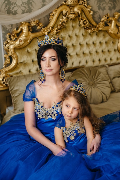 Schöne Prinzessin Mutter und Tochter in einer goldenen Krone und luxuriösen blauen Kleidern