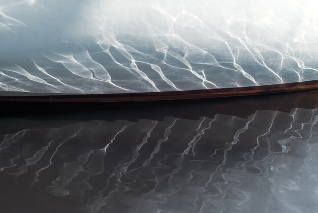 Schöne Reflexionen von Wellen und Sonnenlicht an Bord eines kleinen Segelboots, das in einer bewaldeten Bucht vor Anker liegt