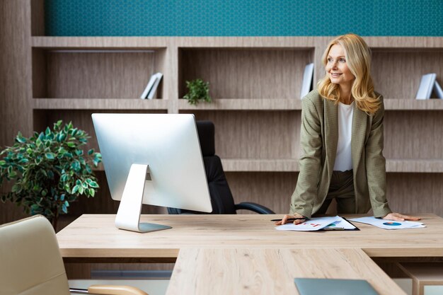 Schöne reife erwachsene Geschäftsfrau mit elegantem Kleid, die am Computertisch im Büro sitzt