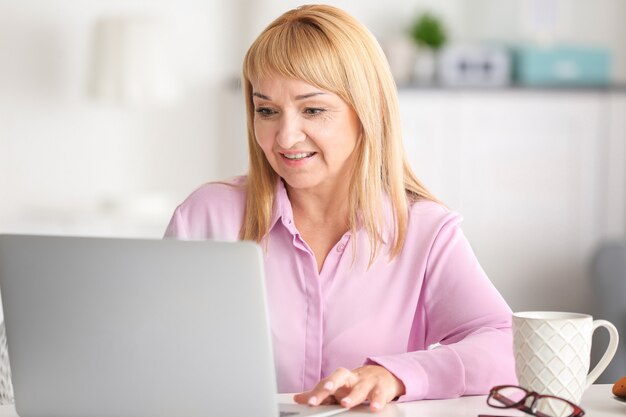 Schöne reife Frau, die zu Hause am Laptop arbeitet