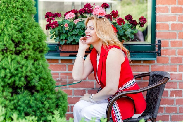 Schöne reife Frau in einem weißen und roten Anzug sitzt auf einer Sommerterrasse