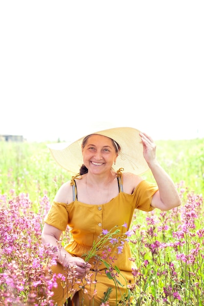 Schöne reife Frau in gelbem Sommerkleid und Strohhut am Sommertag im Feld