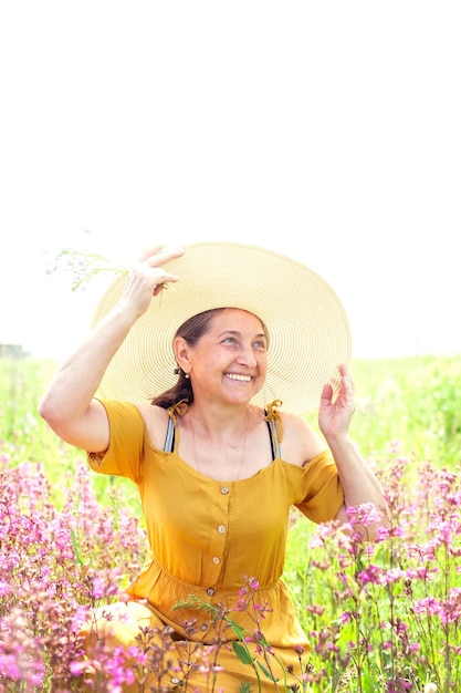 Schöne reife Frau in gelbem Sommerkleid und Strohhut am Sommertag im Feld