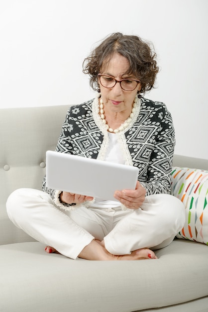 Schöne reife Frau mit einer Tablette auf dem Sofa