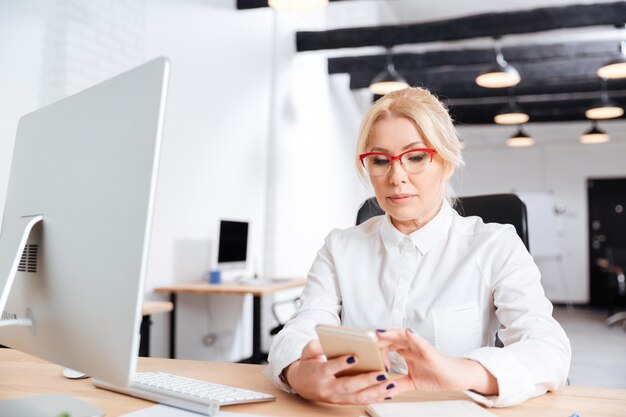 Schöne reife Frau mit Smartphone im Büro