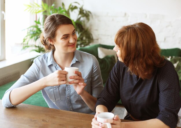 Schöne reife Mutter und ihre erwachsene Tochter trinken Kaffee