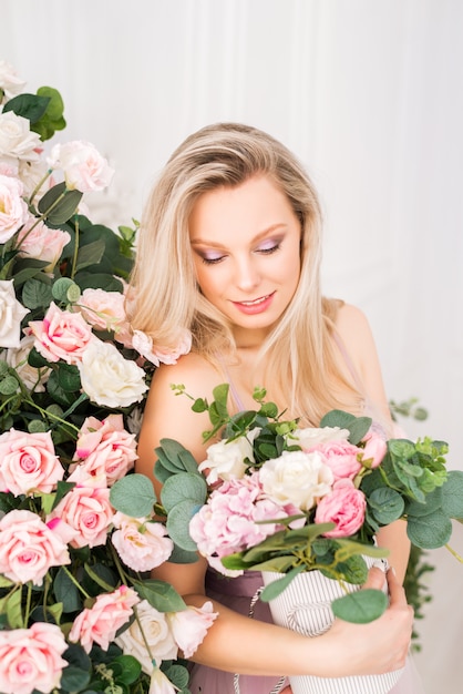 Schöne romantische junge Frau mit natürlichem Make-up. Hellrosa und weiße Rosen mit viel Grün. Parfüm- und Kosmetikkonzept.