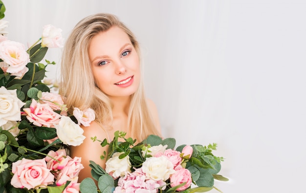 Schöne romantische junge Frau mit natürlichem Make-up. Hellrosa und weiße Rosen mit viel Grün. Parfüm- und Kosmetikkonzept.