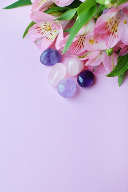 Schöne rosa Alstroemeriablumen und Halbedelsteine Rosenquarz und Amethyst liegen auf einem rosa Hintergrund