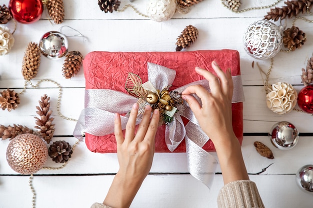 Schöne rosa Geschenkbox in den Händen gegen Details der Weihnachtsdekor-Nahaufnahme.