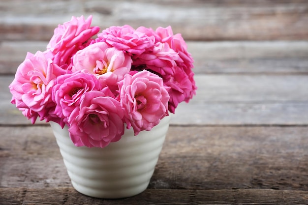 Schöne rosa Rosen im Topf auf hölzernem Hintergrund