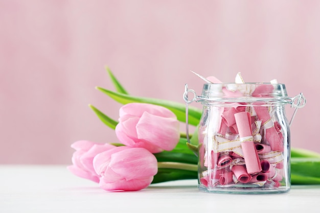 Schöne rosa Tulpen mit Glas Papier auf dem Tisch auf hellem Hintergrund