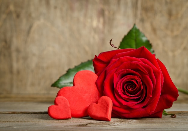 Schöne Rose und drei handgemachte Herzen auf der Holzbrettoberfläche. Herzen aus Salzteig