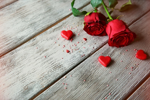 Schöne Rosen mit kleinen Herzen auf Holzhintergrund