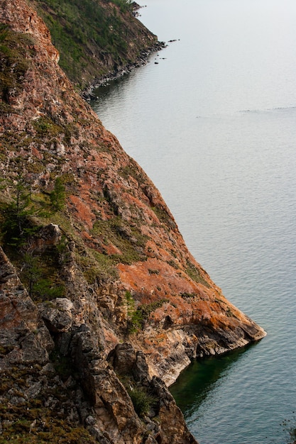 Schöne rote Felsen am Ufer des Baikalsees auf der Insel Olchon. Vertikaler Rahmen. Steile Felsen gehen ins Wasser.