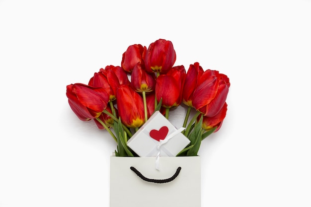 Schöne rote Tulpen in einer Papiergeschenktüte, Geschenkbox mit einem Herzen auf einem weißen