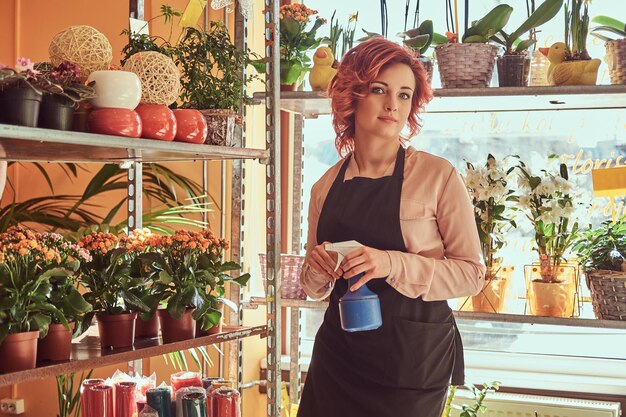 Schöne rothaarige Floristin in Uniform, die in einem Blumenladen arbeitet.