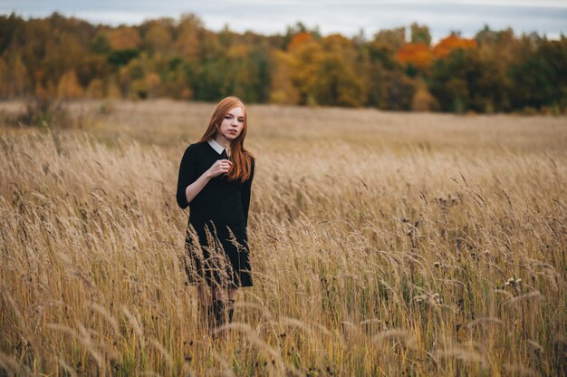 Schöne rothaarige Frau in einem schwarzen Kleid geht auf ein Herbstfeld.