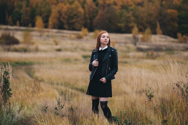 Schöne rothaarige Frau in einem schwarzen Kleid geht auf ein Herbstfeld.