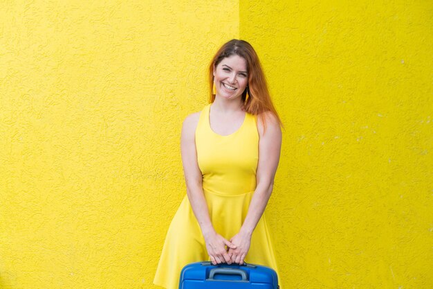 Schöne rothaarige Frau mit einem blauen Koffer auf gelbem Hintergrund