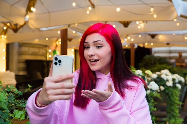 Schöne rothaarige Influencer-Bloggerin im Café, die mit ihren Abonnenten in sozialen Netzwerken Videoanrufe über Smartphone macht.