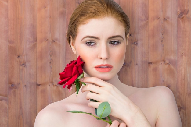 Schöne Rothaarige posiert mit roter Rose gegen Holzbohlen