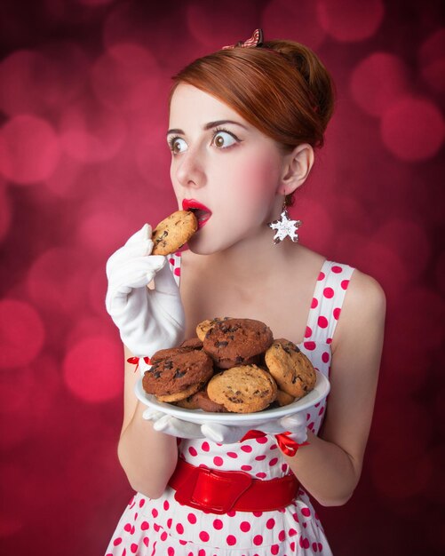 Schöne Rothaarigefrauen mit Coockie. Foto im Retro-Stil mit Bokeh im Hintergrund.