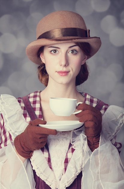 Schöne Rothaarigefrauen mit einer Tasse Tee. Foto im Retro-Stil mit Bokeh im Hintergrund.