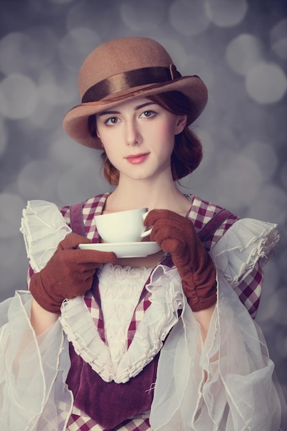 Schöne Rothaarigefrauen mit einer Tasse Tee. Foto im Retro-Stil mit Bokeh im Hintergrund.