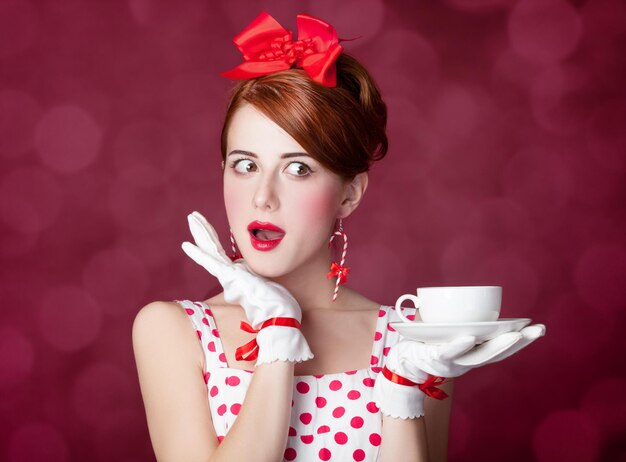 Schöne Rothaarigefrauen mit einer Tasse Tee. Foto im Retro-Stil mit Bokeh im Hintergrund.