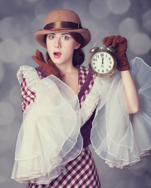 Schöne Rothaarigefrauen mit Uhr. Foto im Retro-Stil mit Bokeh im Hintergrund.