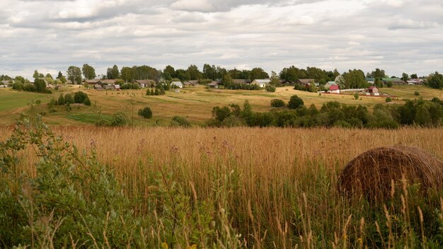 Schöne rustikale Sommerlandschaft mit alten Holzhäusern und Heu auf dem Feld